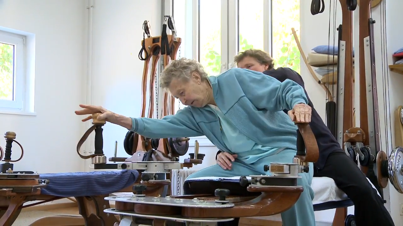 An eldering woman doing Gyrotonic Exercise on the handles